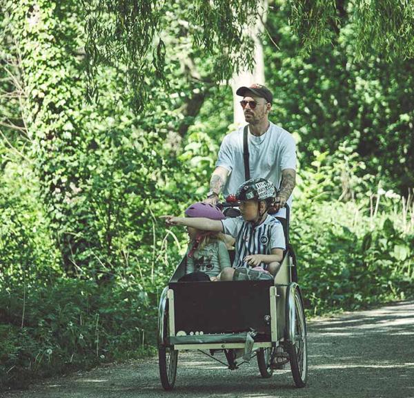 Mand cykler i grønne omgivelser med børn i ladcykel